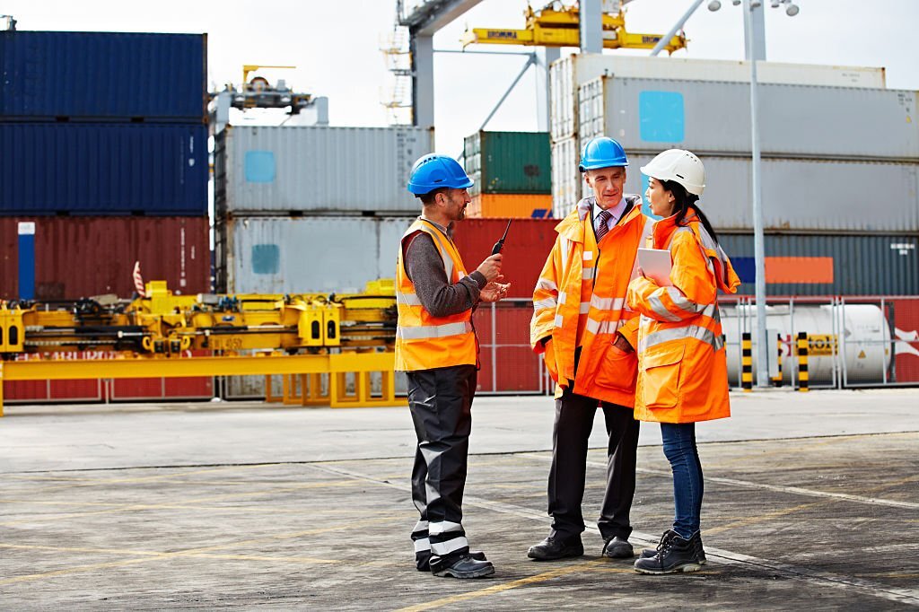 Shot of three workers talking together while standing on a commercial dock